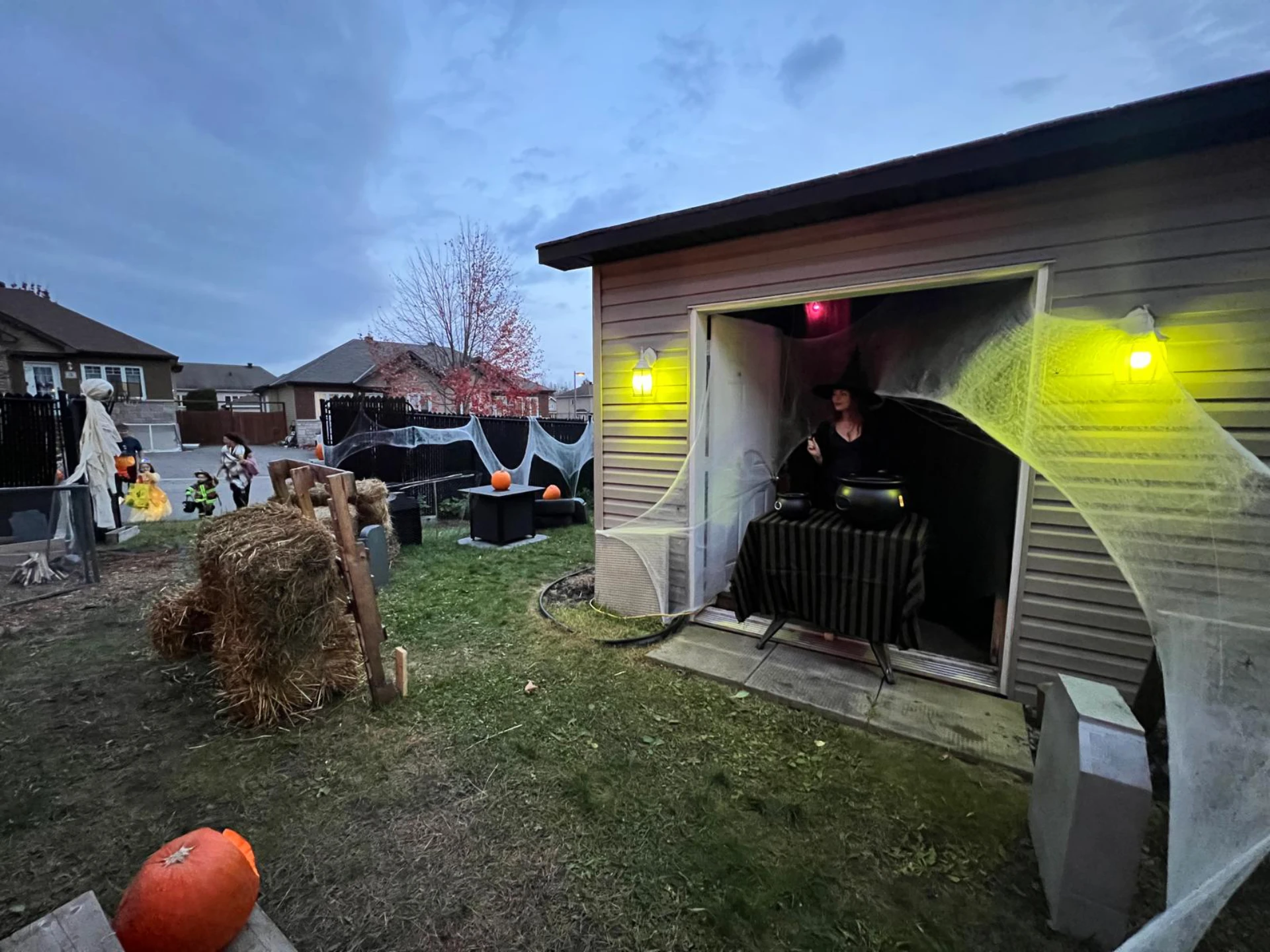 L in the shed at the candy table with trick-or-treaters approaching in the background