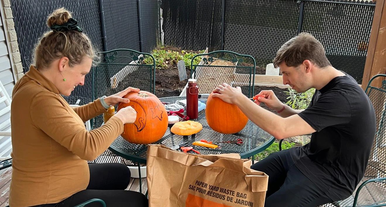 Jenn and Phil carving pumpkins on a patio table