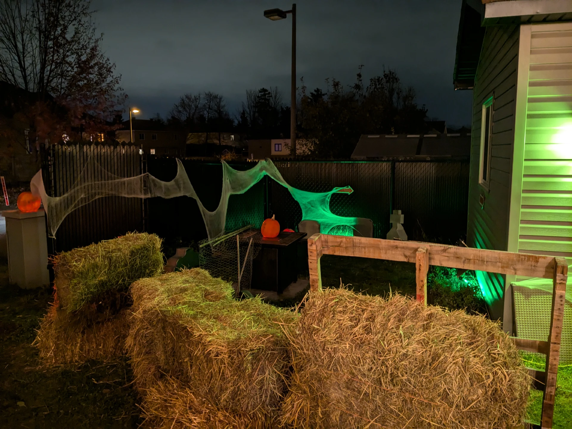 Hay bails forming a wall, with lit jack-o-lanterns, cobwebs, and gravestones in the background