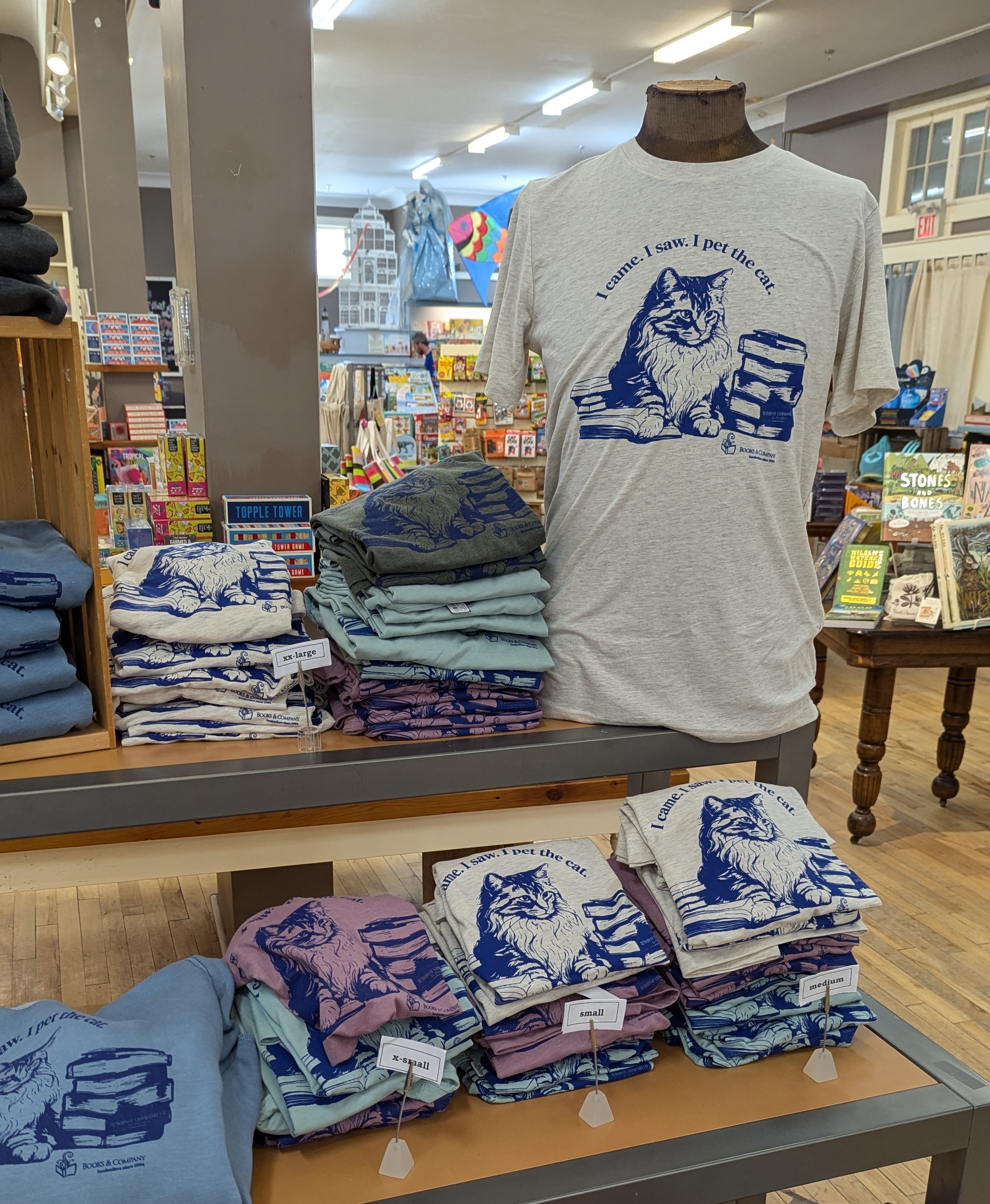 Piles of t-shirts and a mannequin wearing a t-shirt featuring the resident cat and the line 'I came. I saw. I pet the cat.'