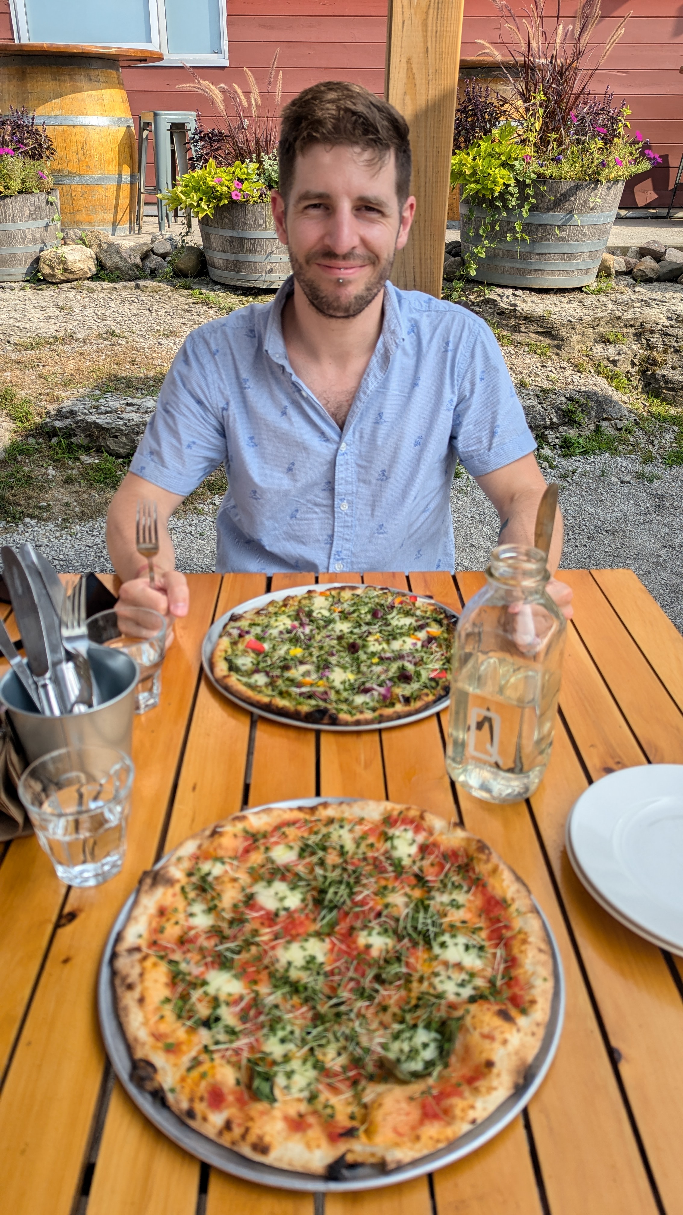 Phil sitting in front of freshly served pizza, fork and knife in hand